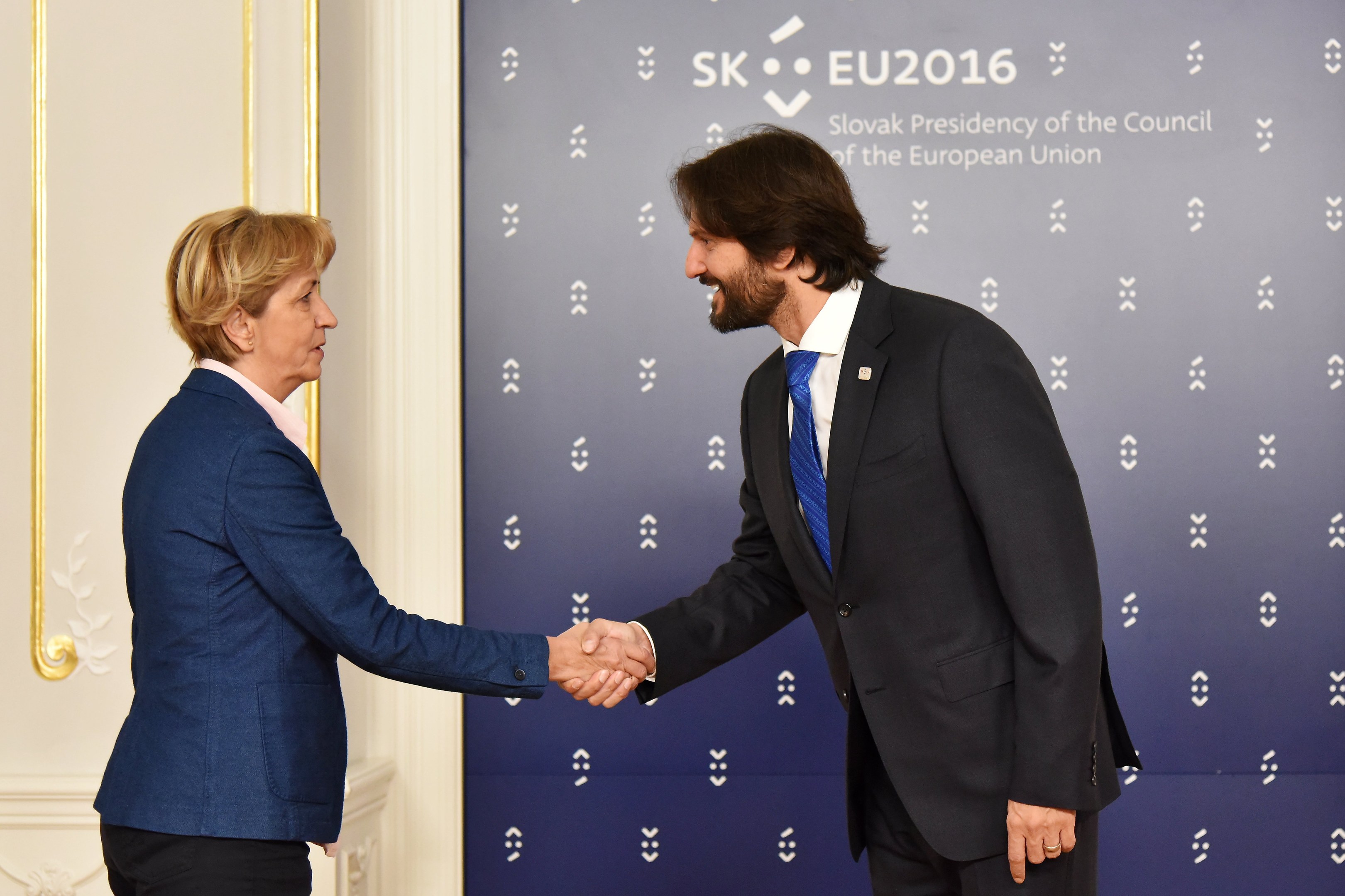 Bundeskanzlerin Angela Merkel und Bundeskanzler Joachim Gauck schütteln sich lachend die Hände vor einem "EU-Gipfel"-Plakat.