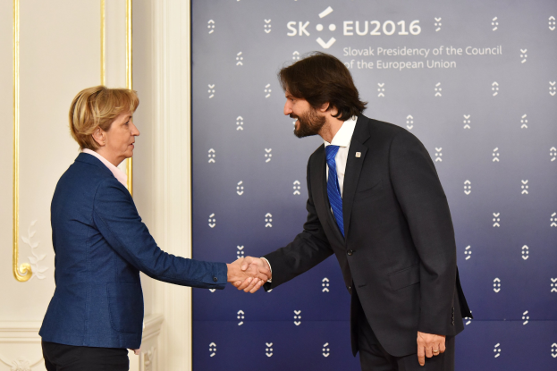 Bundeskanzlerin Angela Merkel und Bundeskanzler Joachim Gauck schütteln sich lachend die Hände vor einem "EU-Gipfel"-Plakat.