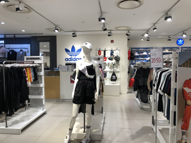 Innenraum eines adidas-Geschäfts in Singapur mit Schaufensterpuppen, Kleiderauslagen, einer Texttafel auf der rechten Seite und Deckenbeleuchtung.