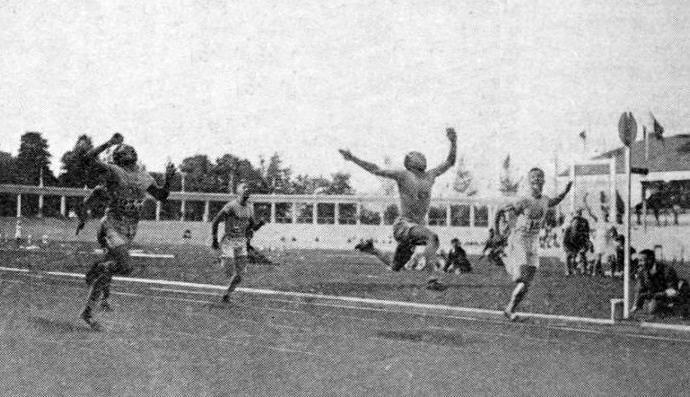 Schwarzes und weißes Foto von Männern, die auf einem Feld Fußball spielen, mit Zuschauern, Pfosten, Fahnen, Gebäuden, Bäumen und einem klaren Himmel, mit dem Text "Sydney Football Club" unten.
