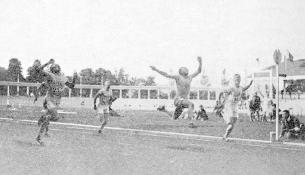 Schwarzes und weißes Foto von Männern, die auf einem Feld Fußball spielen, mit Zuschauern, Pfosten, Fahnen, Gebäuden, Bäumen und einem klaren Himmel, mit dem Text "Sydney Football Club" unten.
