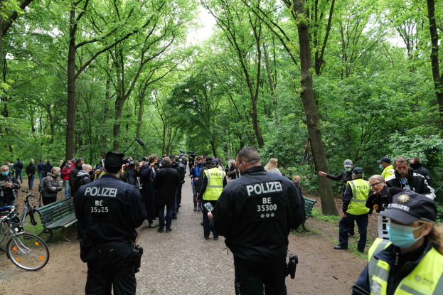 Polizeibeamte vor einer Menge mit Fahrrädern und einer Bank im Vordergrund und Bäumen im Hintergrund bei einer Anti-Terror-Demonstration in Berlin.