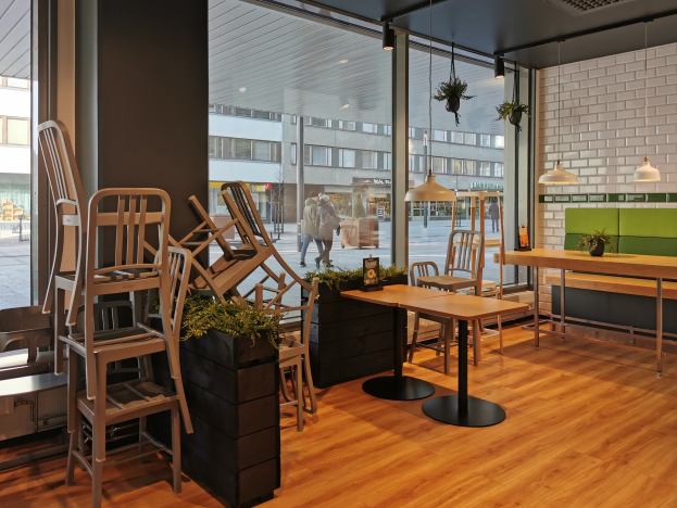 Ein Berliner Restaurant mit hölzernen Tischen und Stühlen in der Nähe eines großen Fensters, das eine Straßenszene im Freien zeigt, mit Fußgängern, Gebäuden und Grünflächen.