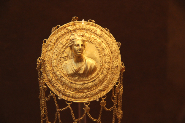 Goldene Medaille mit einer Frauengestalt, die detaillierte Verzierungen zeigt, vor einem dunklen Hintergrund.