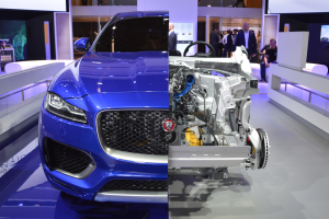 Ein blauer Jaguar F-Pace R-Dynamic S AWD wird auf der Frankfurter Motor Show präsentiert, umgeben von Menschen, die das Auto beobachten und fotografieren, sowie Bildschirmen im Hintergrund.