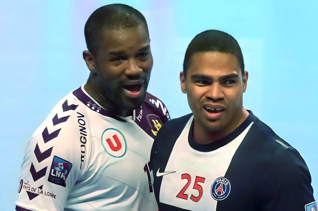 Zwei Männer in weißen und blauen Fußballtrikots stehen nebeneinander auf einem Feld, feiern mit erhobenen Armen vor einem hellblauen Hintergrund.