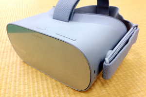 Schwarzer Oculus VR-Headset mit weißen Akzenten auf einem gelben Tisch, mit einstellbaren Riemen und integriertem Mikrofon.