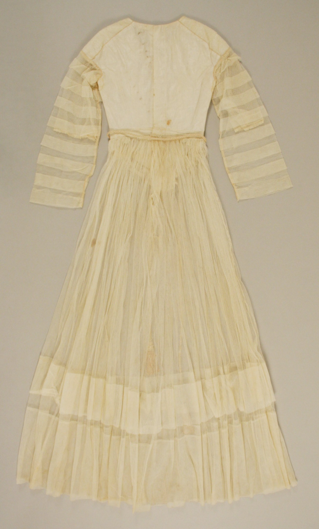 Ein weißes, langärmeliges Kleid mit einer gerüschten, voluminösen Schleppe auf einer weißen Oberfläche, das einen dezenten Glanz und eine hohe Taille aufweist.