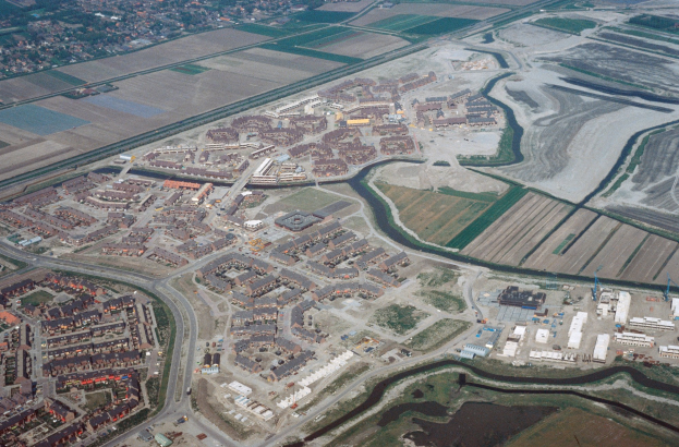 Luftaufnahme einer Stadt mit dichtem Baumbestand, Straßen, Grünflächen, Bäumen und einem zentralen Reservoir, umgeben von städtischen und natürlichen Bereichen.