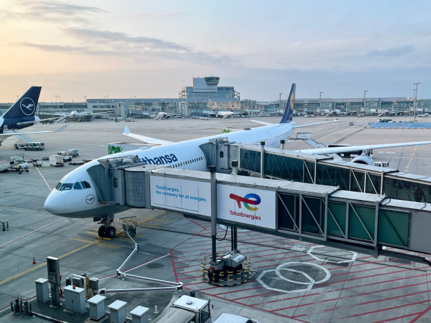 Ein großes Passagierflugzeug auf dem Rollfeld eines Flughafens umgeben von anderen Flugzeugen, Fahrzeugen und Gebäuden unter einem klaren blauen Himmel.