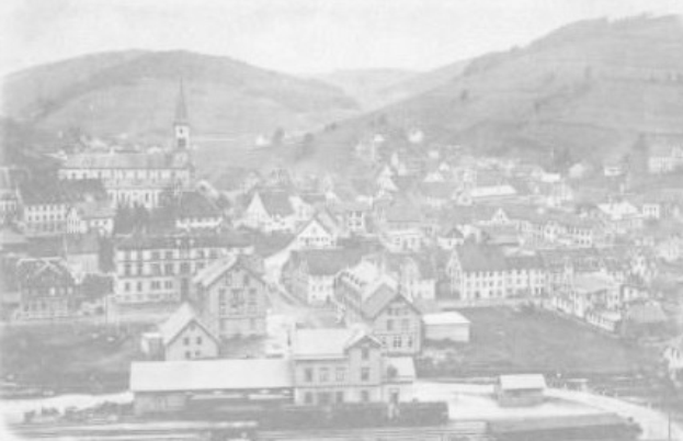 Schwarzes und weißes Foto von Lauterbrunnen, Deutschland im 19. Jahrhundert, das eine Stadt mit vielen Gebäuden, Hügeln und einem Himmel im Hintergrund zeigt.