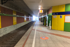 Ein Bahnhofsgebäude in Berlin, Deutschland, mit einem Zug auf den Gleisen, beleuchtet von Deckenlampen, Graffiti an der linken Wand und ein paar Gegenständen auf der rechten Seite.