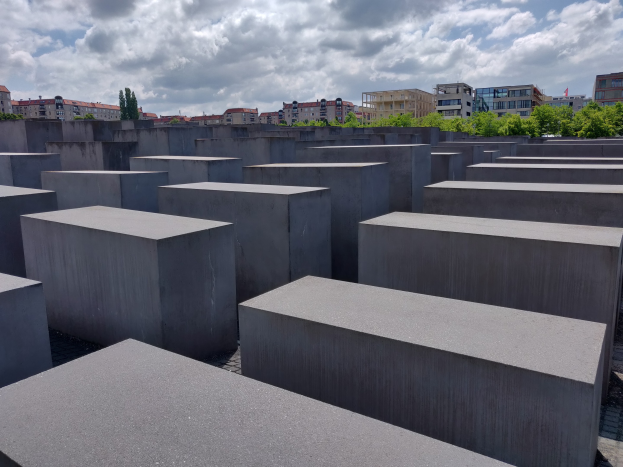 Konkreter Holocaust-Mahnmal in Berlin, Deutschland, mit Bäumen, Gebäuden und Wolken im Hintergrund.