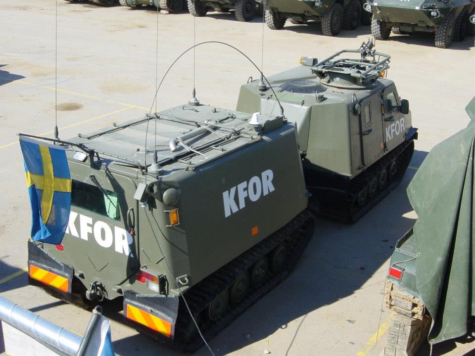Gruppe gepanzerter Militärfahrzeuge auf einem Parkplatz geparkt, mit einem Metallzaun links und einer Flagge an einem Fahrzeug.