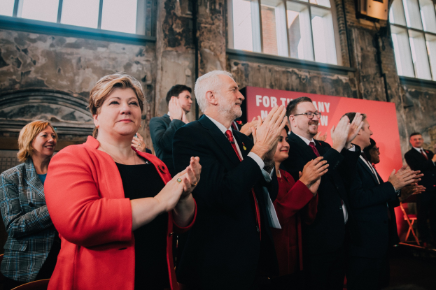 Eine Gruppe von Menschen, die vor einem Publikum jubeln, mit einem Banner im Hintergrund, das einen Wahlsieg anzeigt.