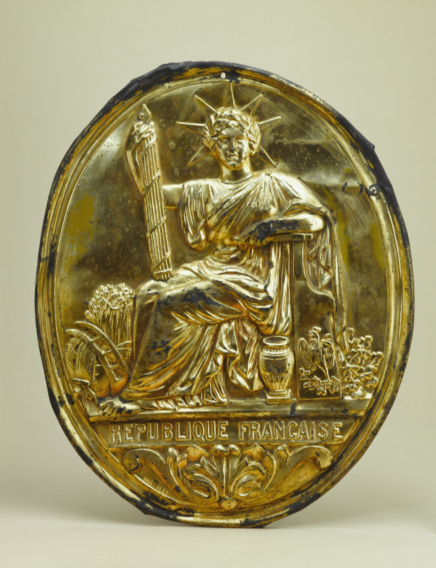 Goldenes rundes Schild mit einer erhabenen Statue der Freiheitsstatue und eingraviertem Text auf weißem Hintergrund.