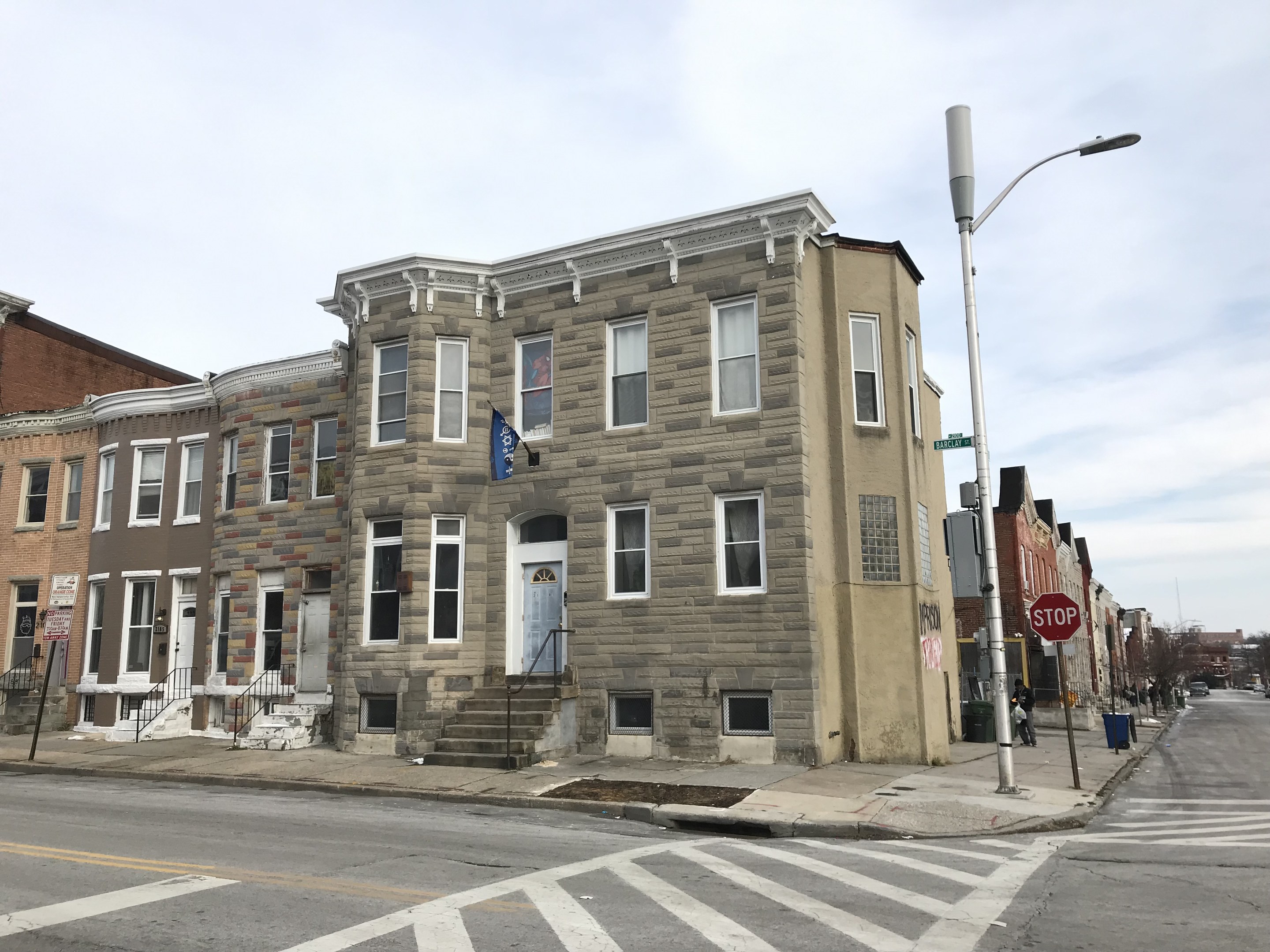 Eine Reihe moderner Häuser mit Fenstern, Türen, Treppen mit Geländern und Laternen an einer Straßenkreuzung in Philadelphia, mit Fahrzeugen auf der Straße, Bäumen und einem bewölkten Himmel im Hintergrund.