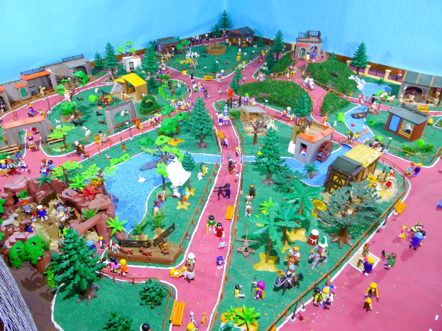 Zoo-Modell mit zahlreichen Besuchern, umgeben von Bäumen, Häusern, Pflanzen, Gras, einem Zaun und anderen Gegenständen, mit einer Hintergrundwand und Text unten.