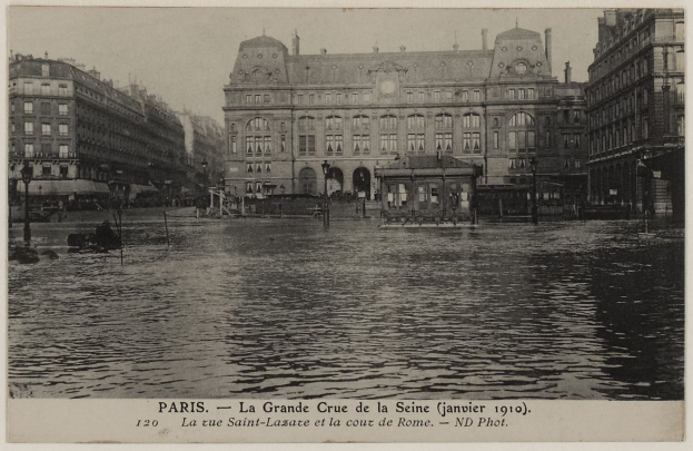 Schwarz-weiß-Foto einer überfluteten Straße in Paris mit Gebäuden, Straßenlaternen, Lichtern, Fahrzeugen und Himmel, mit Text am unteren Rand.