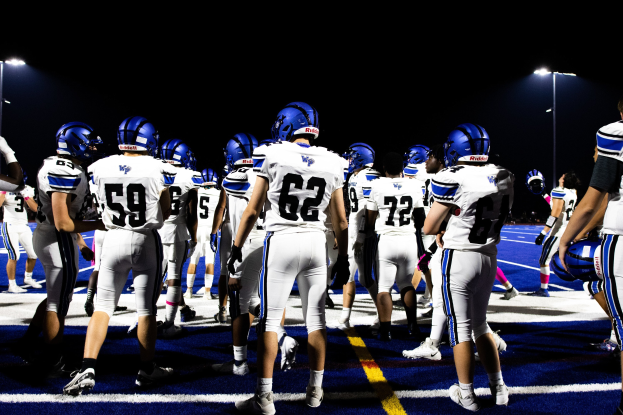Eine Gruppe von Fussballspielern in Helmen und Stiefeln, die auf einem Feld unter Flutlicht stehen.