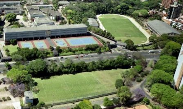 Luftbild eines Fußballfeldes auf dem Campus der Universität Sydney, umgeben von Bäumen, Gebäuden und Fahrzeugen, mit einem neuen Sportkomplex im Bau.