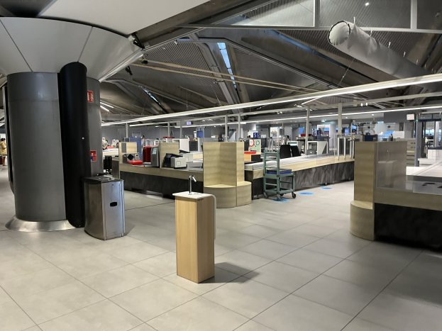 Großer Raum mit mehreren Tischen, Stühlen, Mülltonnen, Maschinen, Säulen und Deckenleuchten im neuen Terminal am Frankfurt Airport, mit sichtbarer Decke und einigen anwesenden Personen.