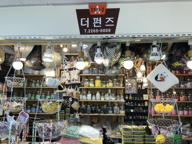 Ein unordentlicher Laden in Seoul mit verschiedenen Gegenständen wie Körben, Lampen, Flaschen und Spielzeugen auf Regalen, mit einem Schild oben, das darauf hinweist, dass es einer der besten koreanischen Läden ist.
