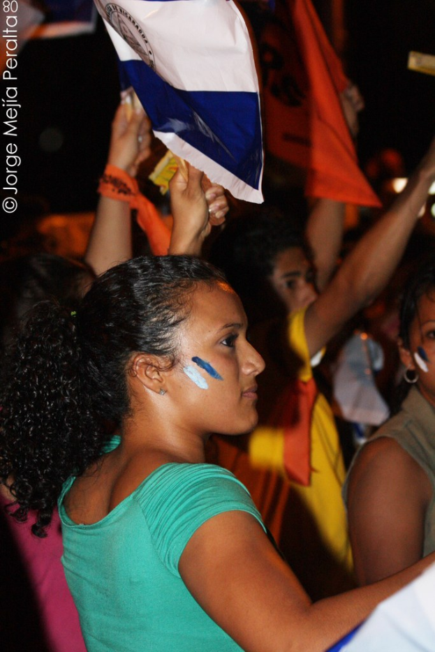 Frauen in grünen T-Shirts bei einer Protestaktion, die weiße Decken halten, mit vielen anderen Mädchen im Hintergrund.