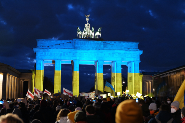 Menschenmenge mit Fahnen und Plakaten vor dem Brandenburger Tor in Berlin, mit einer Banner auf der rechten Seite des Bildes.