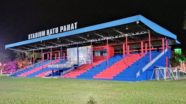 Nachtansicht eines Stadions in Batu Pahat, beleuchtet von Lichtern, umgeben von Bäumen, mit grasbewachsenem Boden und Treppen zum Eingang.
