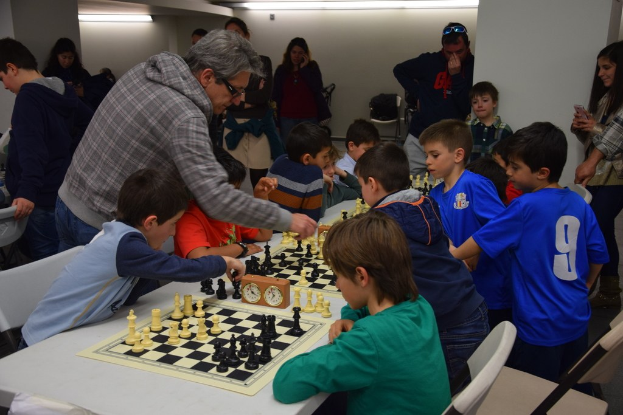Kinder beim Schachspielen in einem Wettbewerb, beobachtet von Erwachsenen im Hintergrund.