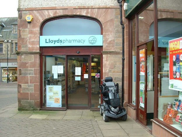 Apotheke mit einem vor dem Gebäude geparkten Fahrzeug und einem Gebäude in der linken Ecke.