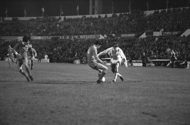 Schwarzes und weißes Foto von Männern, die Fußball in einem Stadion mit Zuschauern in den Rängen und Fahnen im Hintergrund spielen.