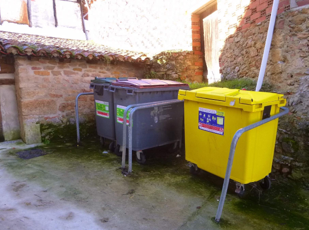Zwei gelbe und graue Recyclingtonnen auf Rädern nebeneinander vor einem Gebäude mit einer Wand und einem Fenster.