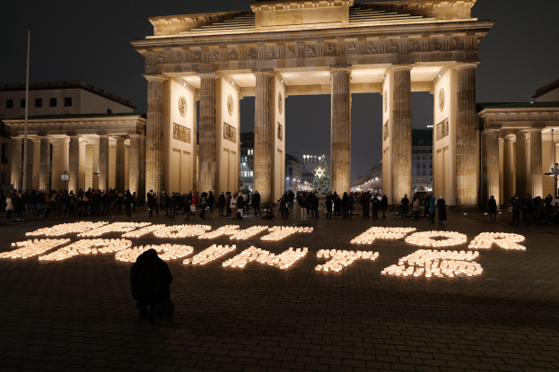 Eine Gruppe von Menschen steht vor dem beleuchteten Reichstagsgebäude in Berlin, Deutschland, umgeben von Gebäuden, Pfählen und Lichtern; die Wörter 'Kampf für die Freiheit' sind auf dem Boden zu sehen.