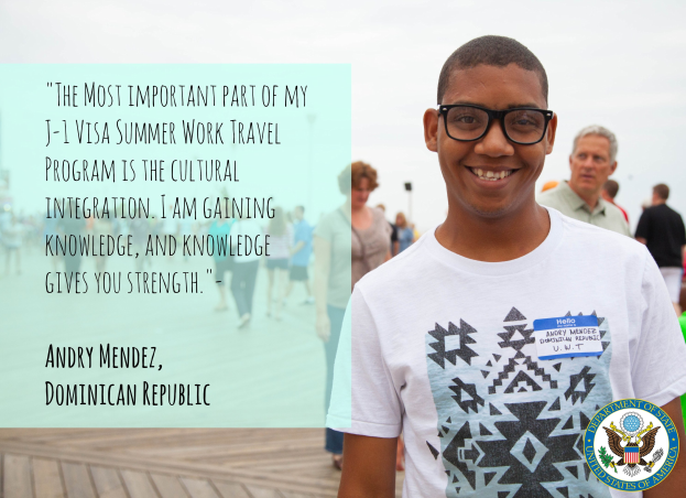 Eine Person in einem weißen T-Shirt lächelt umgeben von einer Gruppe von Menschen, die auf einer hölzernen Oberfläche gehen, mit einem Zitat von Andry Mendez über kulturelle Integration und Wissen im Vordergrund und Gebäuden und einem klaren blauen Himmel im Hintergrund.