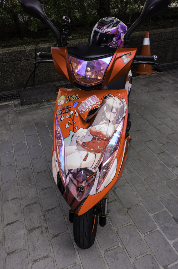 Orangeroller auf einer Straße mit einem Helm darauf, einer Verkehrskegel, einer Wand und Bäumen im Hintergrund.
