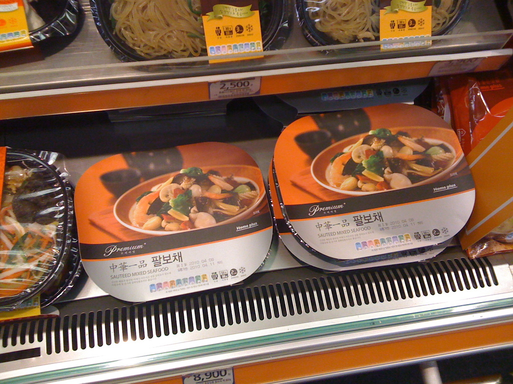 Lebensmittelkisten auf Regalen mit Preiszetteln.