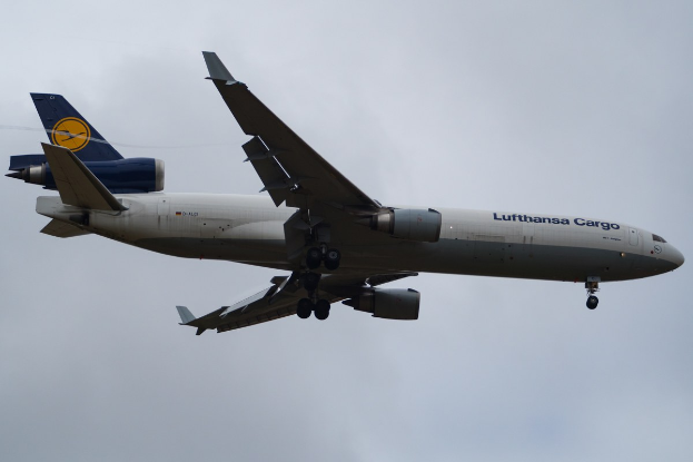 Ein Lufthansa Cargo Boeing 777-300ER im Flug, mit ausgebreiteten Flügeln und Motoren gegen einen bewölkten Himmel, mit dem Text auf dem Rumpf.