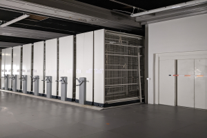 Ein großer Raum voller Numerous Server, mit einem Boden, einer Wand auf der rechten Seite und einer Decke mit Leuchten oben, der wie ein Rechenzentrum aussieht.