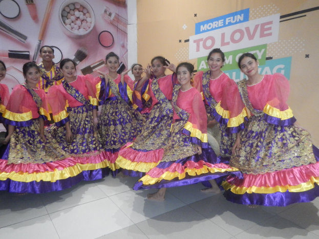 Eine Gruppe junger Frauen in bunten Kleidern, die strahlend und posend vor einem Banner mit Text und Bildern stehen, wahrscheinlich bei der Präsentation einer neuen Schönheitsmarke.