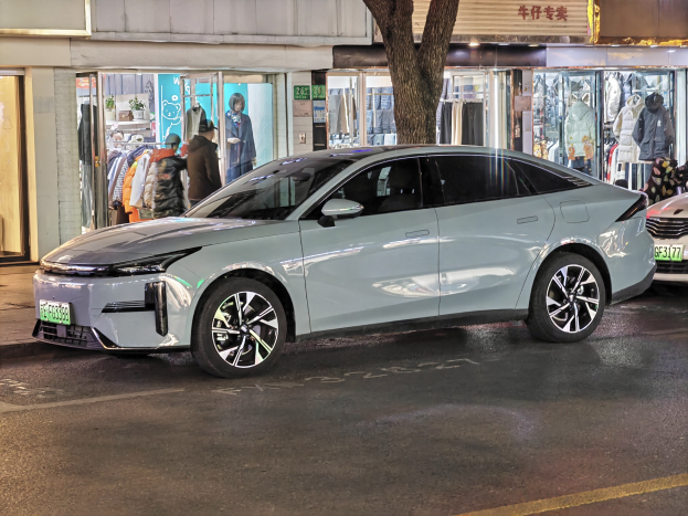 Elektrischer Mitsubishi Lancer EV auf einer nächtlichen Stadtstraße geparkt, umgeben von beleuchteten Schaufenstern, Schaufensterpuppen und Schildern.
