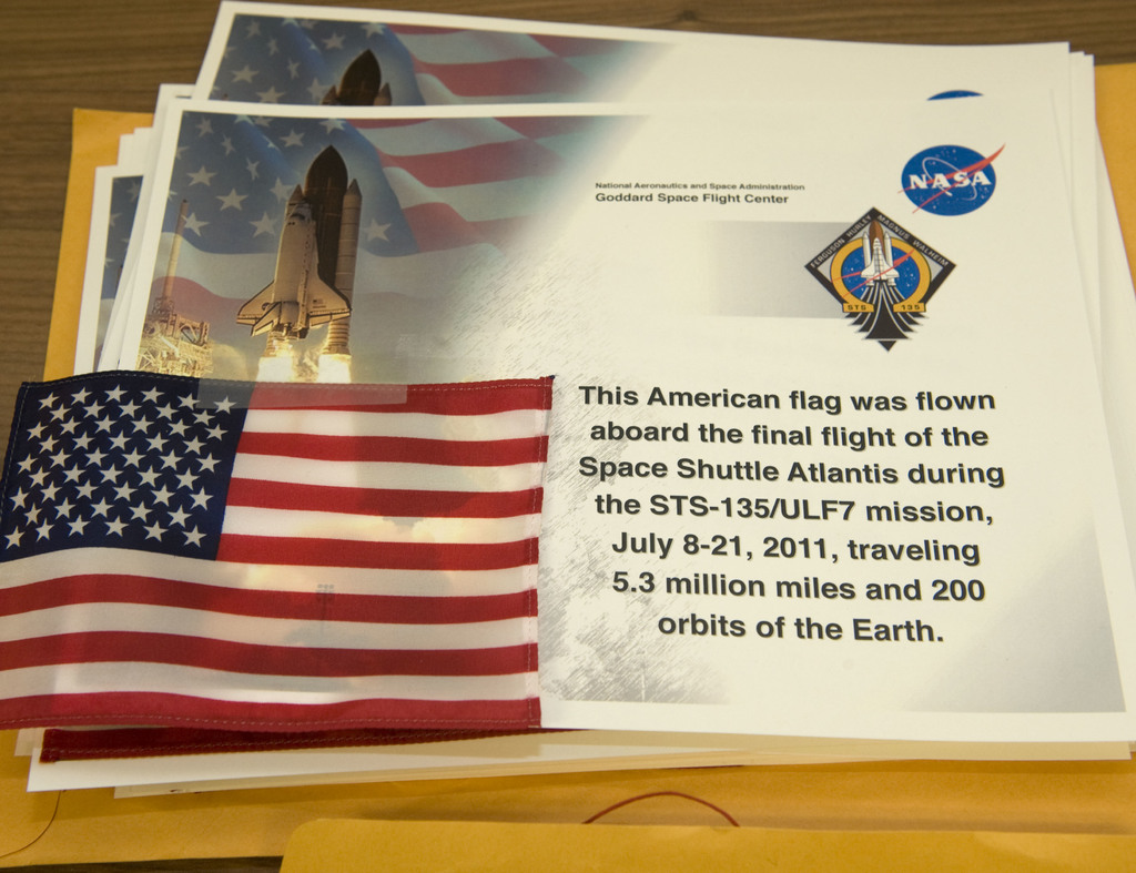 Poster mit Text, einer Flagge, einer Rakete und Logos auf einem Tisch, mit einem Boden oben im Bild.