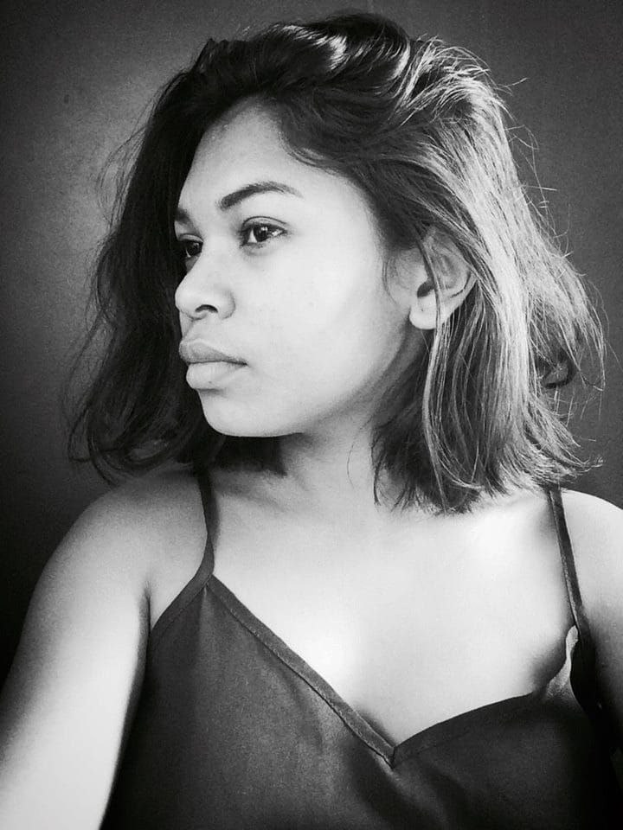 Eine selbstbewusste Frau in einem schwarzen Kleid posiert in einem Schwarz-Weiß-Foto vor einer Wand mit einem glatten Bob und natürlichem Make-up.