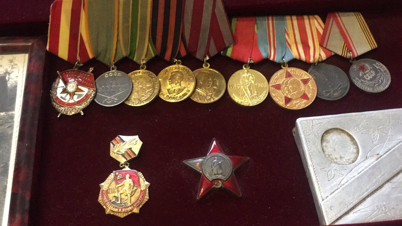 Eine hölzerne Kiste mit verschiedenen Medaillen, darunter ein roter Stern als Symbol der Sowjetunion, ordentlich mit einem Objekt auf der rechten Seite.