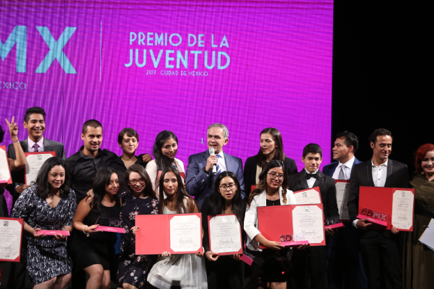 Gruppe von Menschen auf einer Bühne mit Zertifikaten, Mann spricht in ein Mikrofon und ein Bildschirm zeigt "Premio de la Juventud 2017" im Hintergrund.