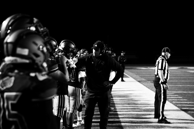 Schwarzes und weißes Foto einer Gruppe von Football-Spielern in Helmen und Sneakers, die auf einem Feld stehen.