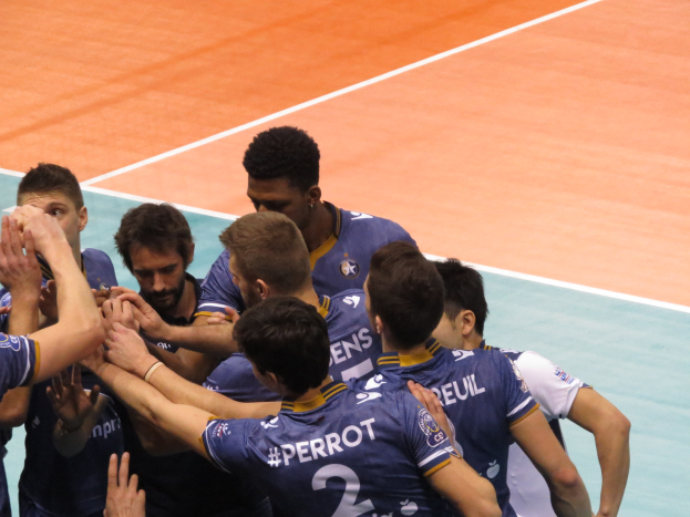 Eine Gruppe von Männern in blauen "Ligue 1"-T-Shirts feiert auf einem Volleyballfeld, einige halten die Hände siegreich hoch.