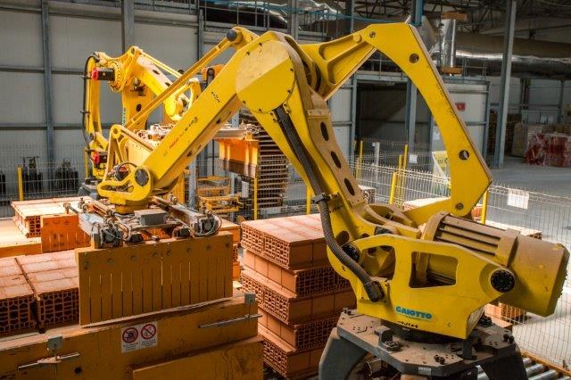 Großes Industriegelände mit gestapelten Kisten, Kränen, Zaun, Strommasten und einer fernen Wand in einer Fertigungsanlage.