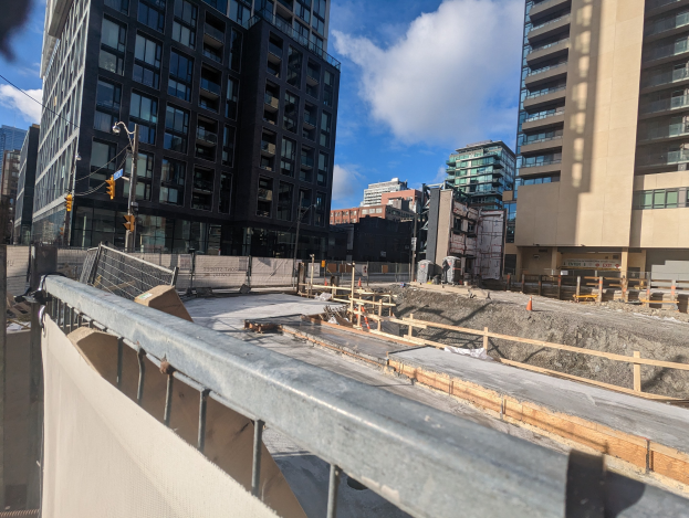 Baustelle in Toronto, Ontario mit einem großen Gebäude im Bau, umgeben von Geländern, Pfählen, Verkehrssignalen und Brettern unter einem bewölkten Himmel.